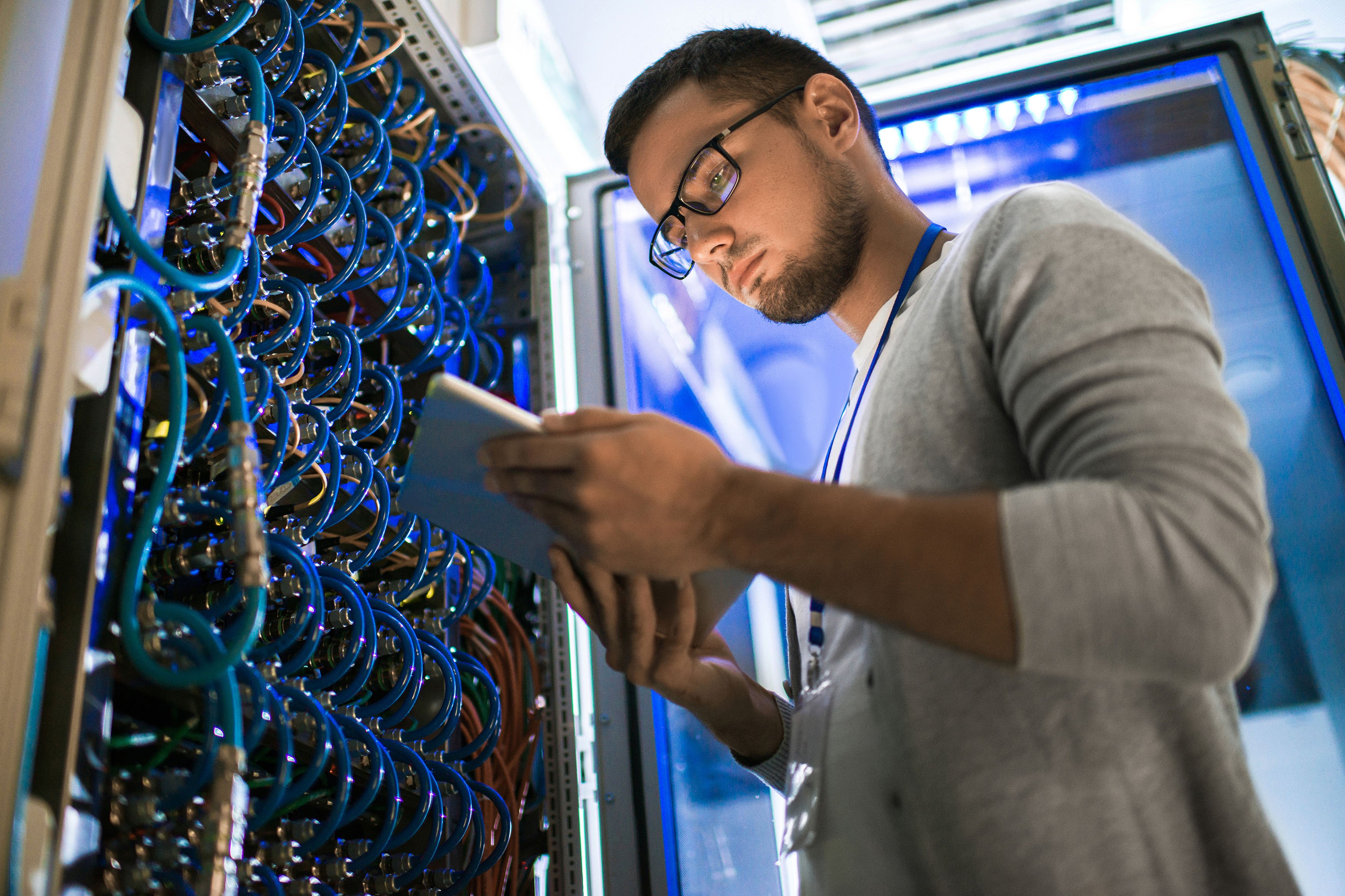 Young man using digital tablet standing by server cabinet