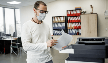 Man wearing a face mask handles printer documents