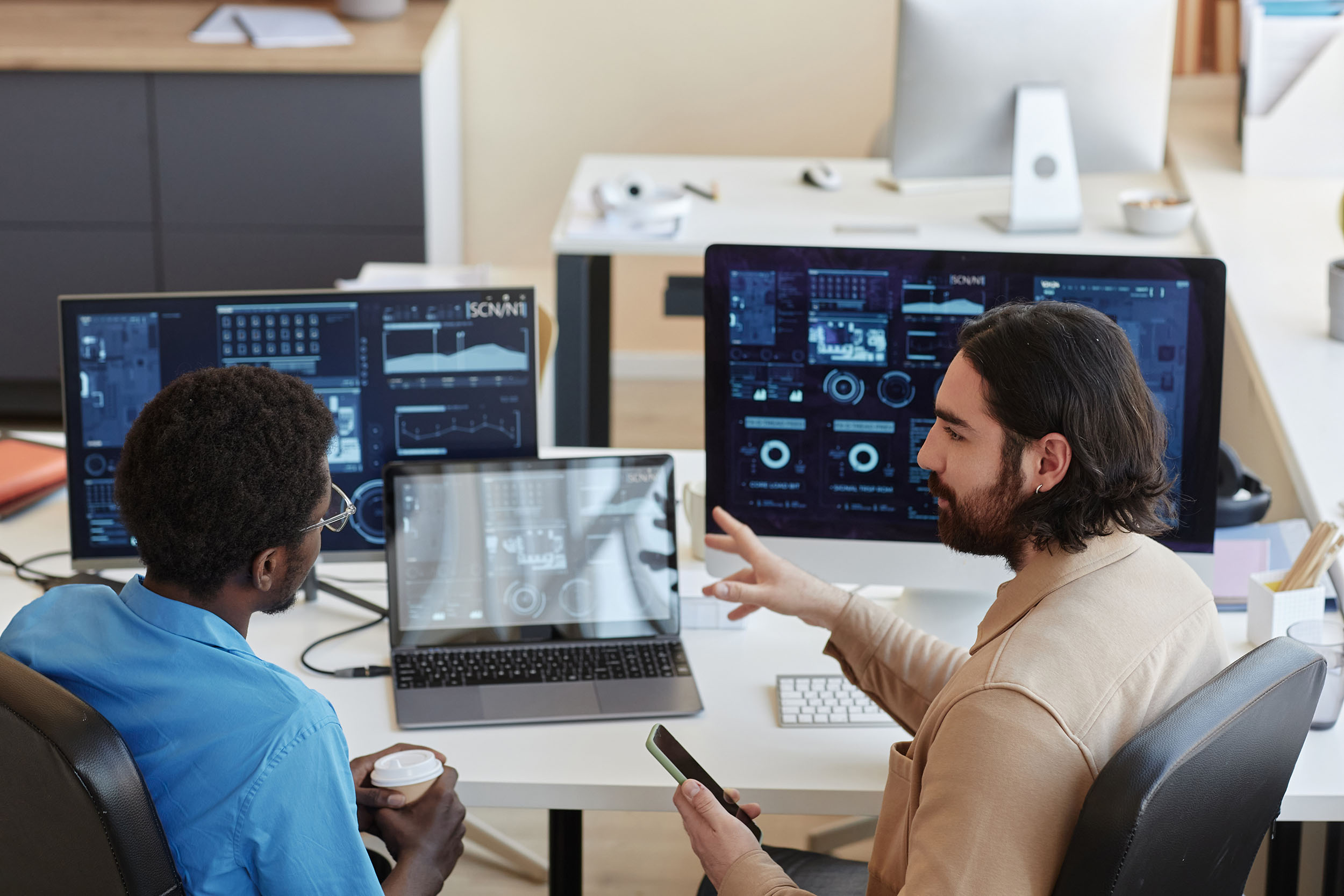 Young confident IT engineer explaining graphic data on computer screens to his colleague